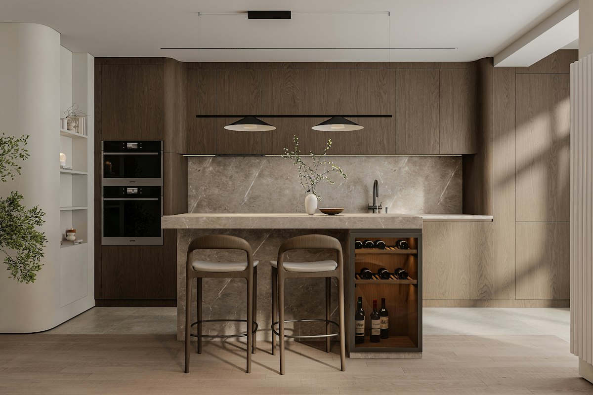A kitchen island with a built-in wine cooler holding bottles beside a wall of dark wood cabinetry and wall ovens