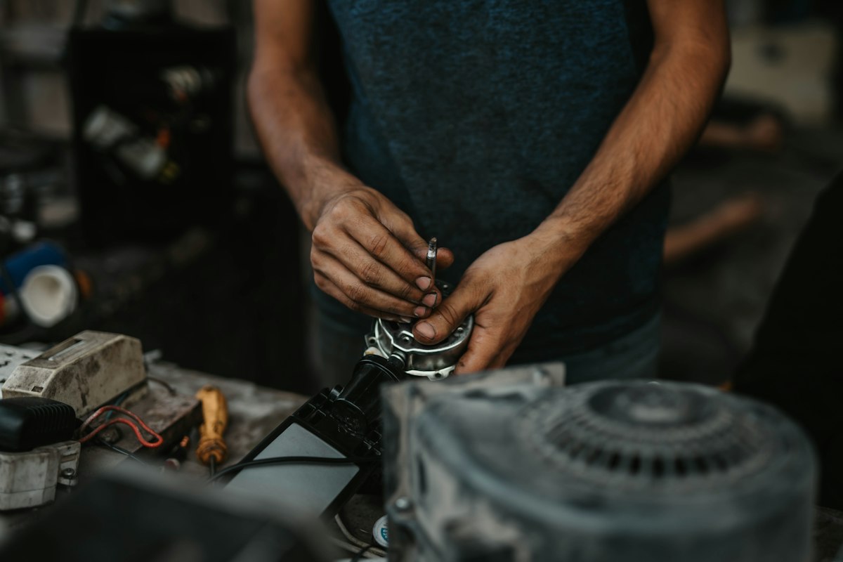 A technician's hands using a screwdriver to inspect an appliance motor assembly on a workbench