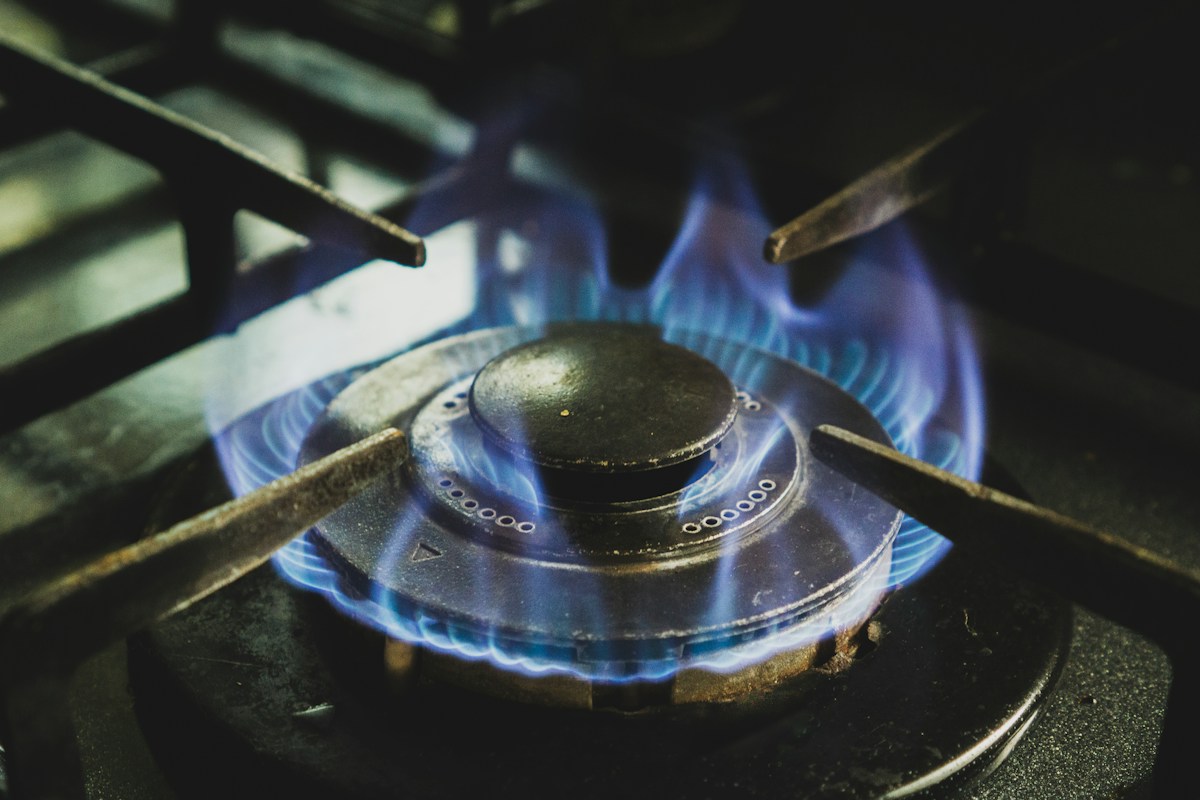 A close-up of a lit gas stove burner with a blue flame ring beneath cast iron grates