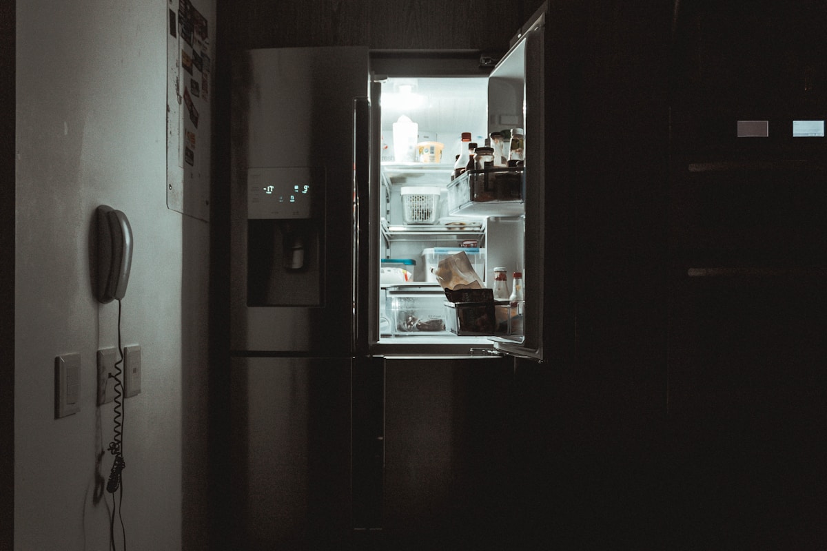 An open refrigerator glowing in a dark Doral kitchen as a homeowner checks why it is not cooling