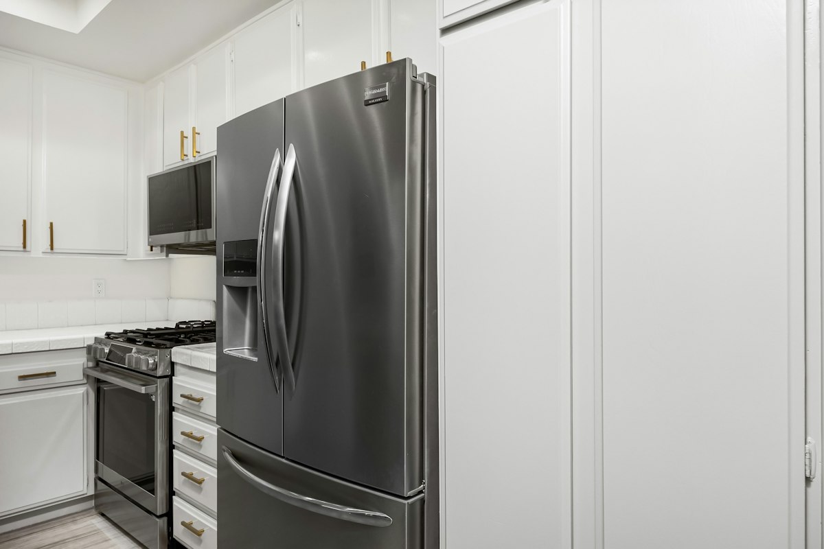 A stainless steel french door refrigerator with an ice and water dispenser in a bright white kitchen