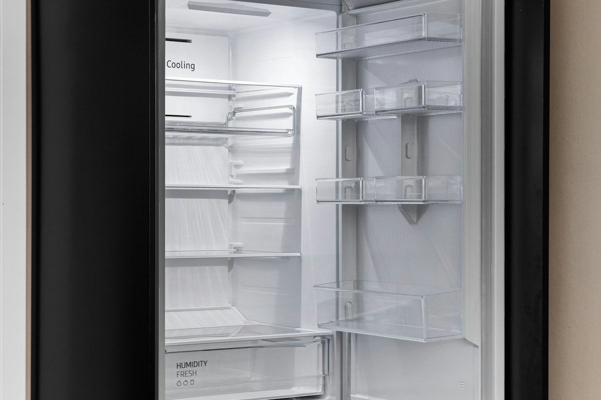 The interior of an empty built-in refrigerator with glass shelves and a Cooling control panel visible on the back wall