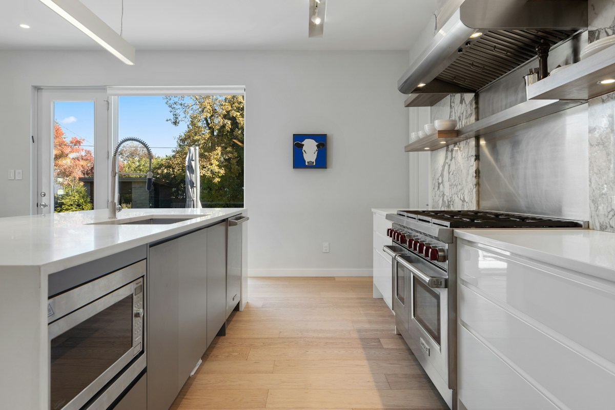 A bright estate kitchen with a professional-style stainless steel dual oven range, red control knobs, and a stainless hood