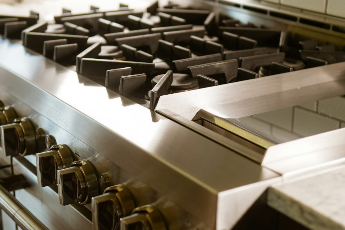 A close-up of a stainless steel rangetop with heavy cast iron grates and a row of control knobs
